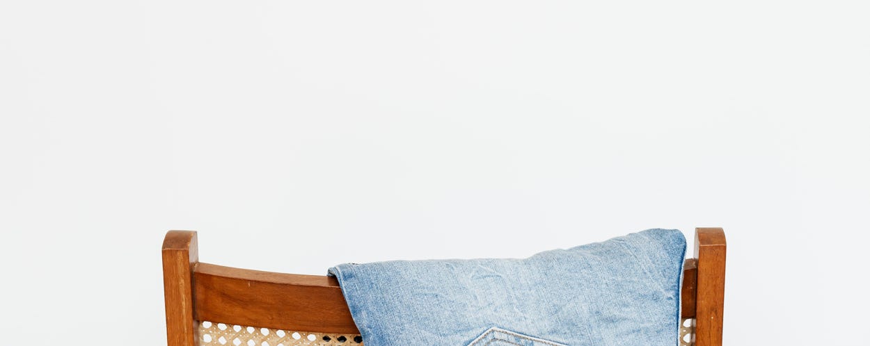 Trendy blue jeans put on back of wooden chair near empty white wall